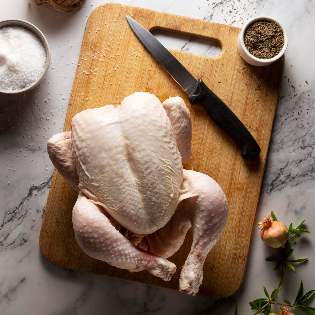 Raw chicken on a wooden cutting board with a knife, salt, and herbs on a marble surface.
